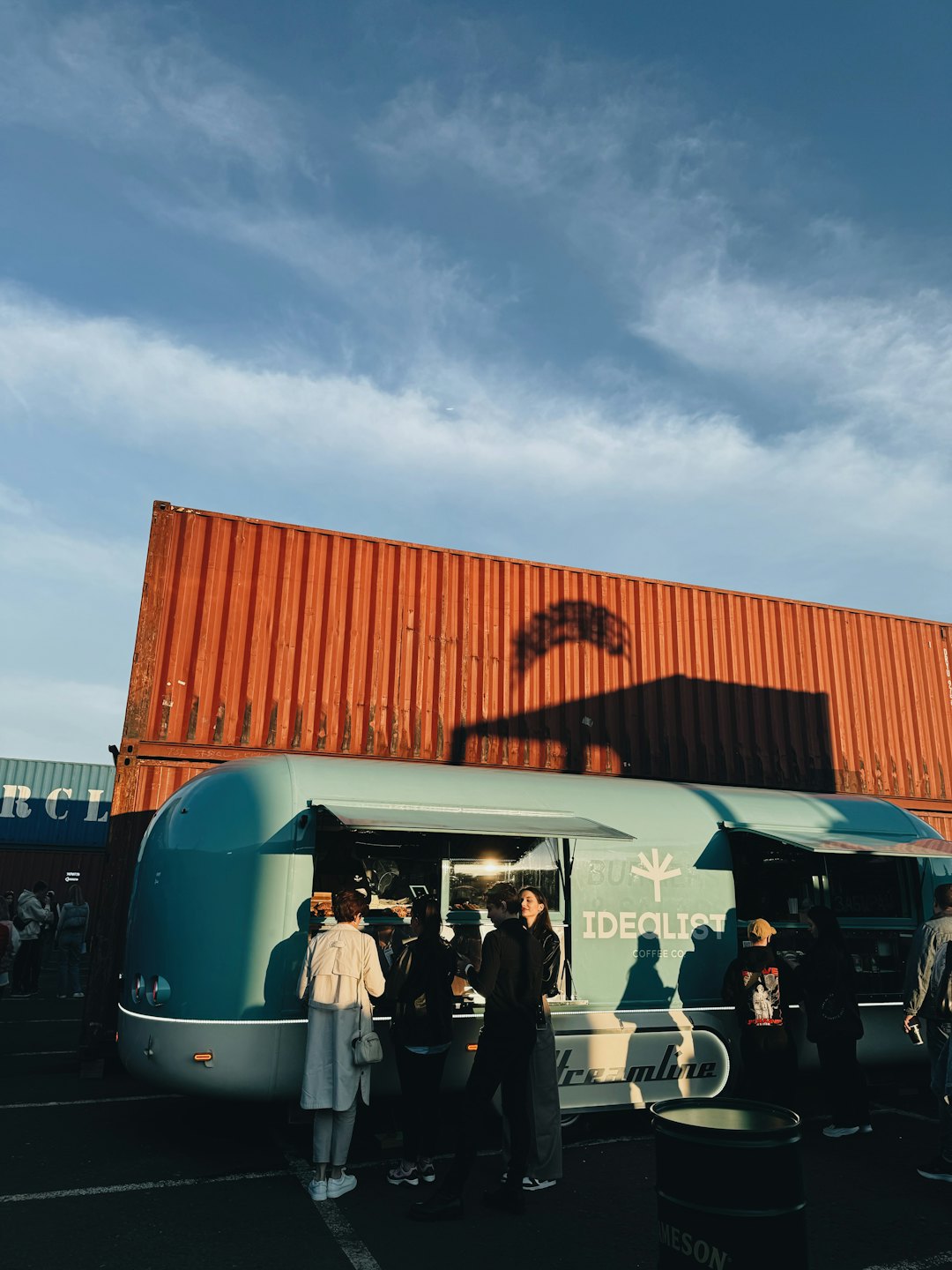 Mensen socialiseren bij een blauwe foodtruck met oranje bakken.