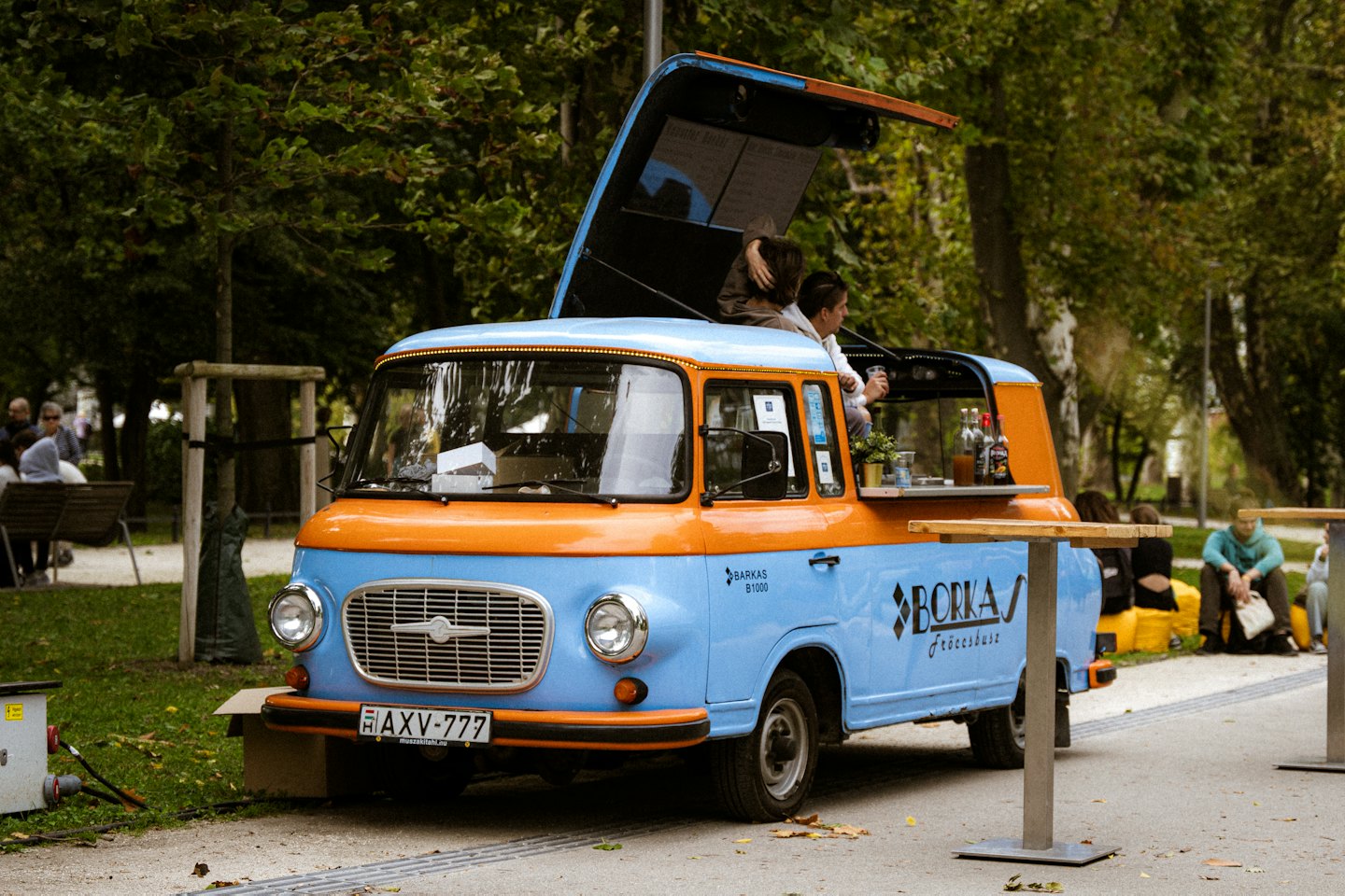 Een vintage foodtruck serveert drankjes buiten bij groene bomen.