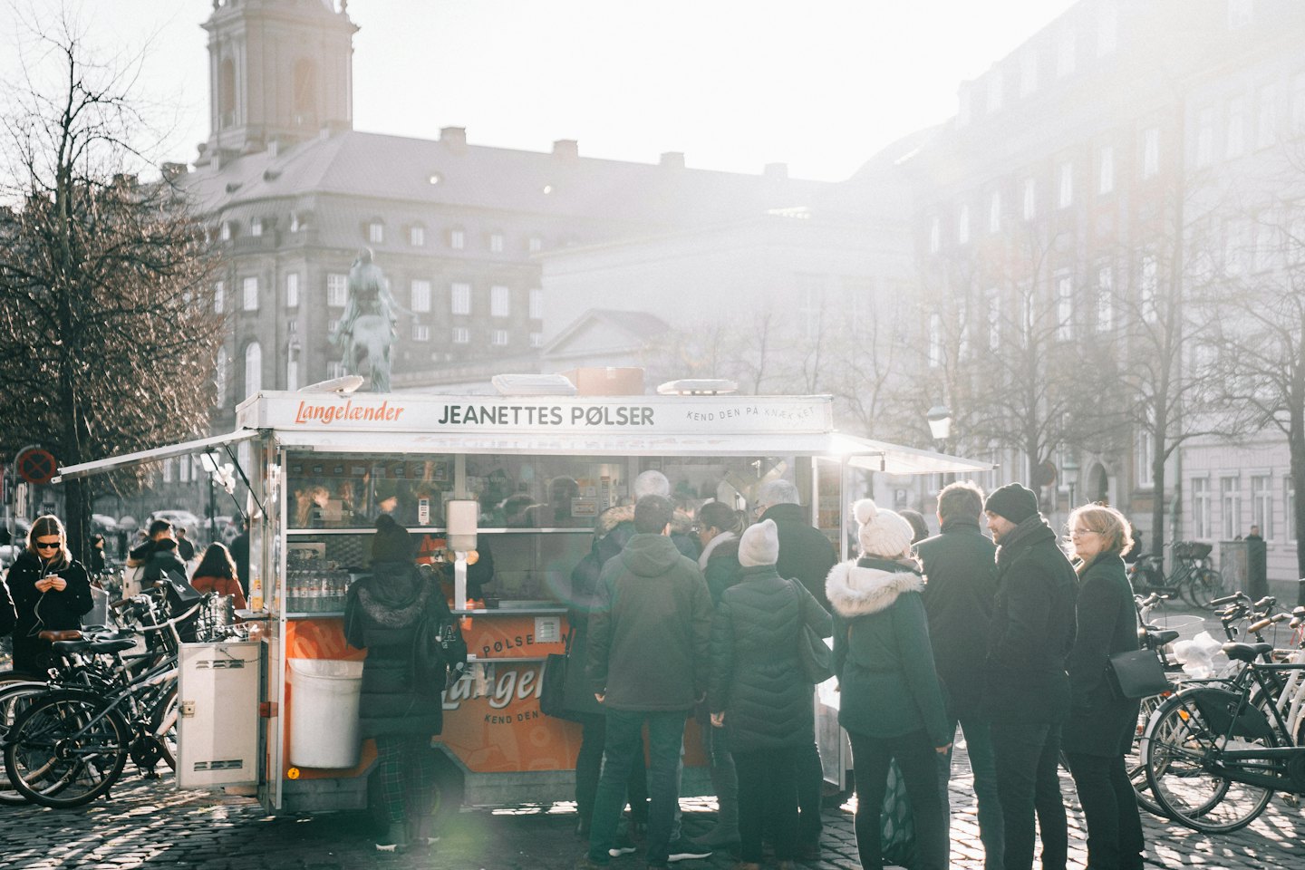 Mensen staan in de rij bij een witte foodtruck op een kasseienstraat.
