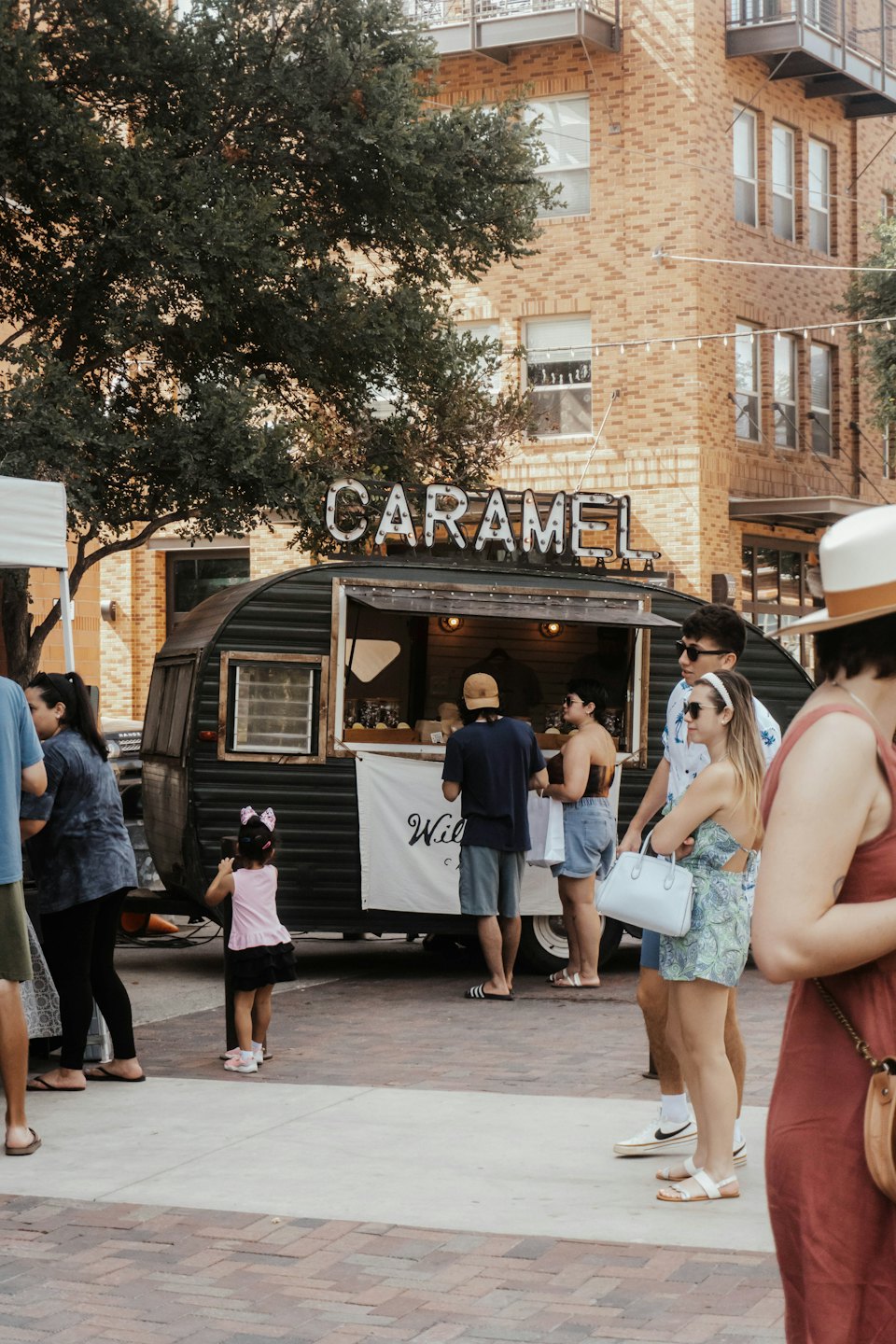 Mensen staan in de rij bij een groene foodtruck met een "CARAMEL"-bord.