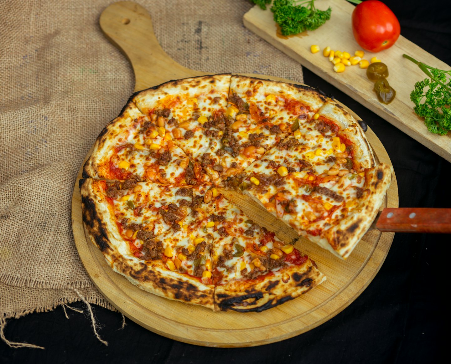 Een spatel tilt een plak pizza van een houten plank.